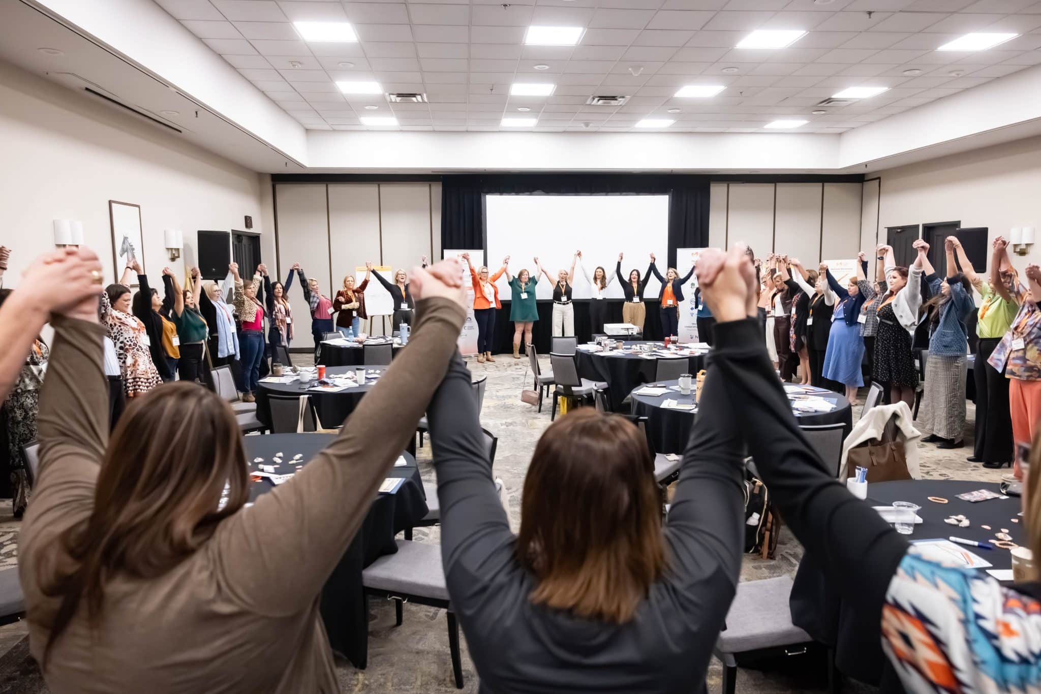 A room full of women in the Women's Leadership Academy raising their hands together